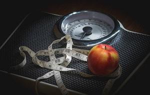 A weight scale with a tape measure and apple on top of it